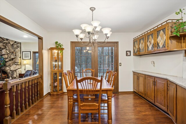 dining area featuring a notable chandelier, dark wood-type flooring, and a stone fireplace