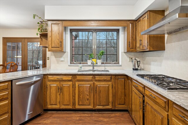 kitchen featuring stainless steel appliances, sink, light stone counters, wall chimney exhaust hood, and dark hardwood / wood-style flooring