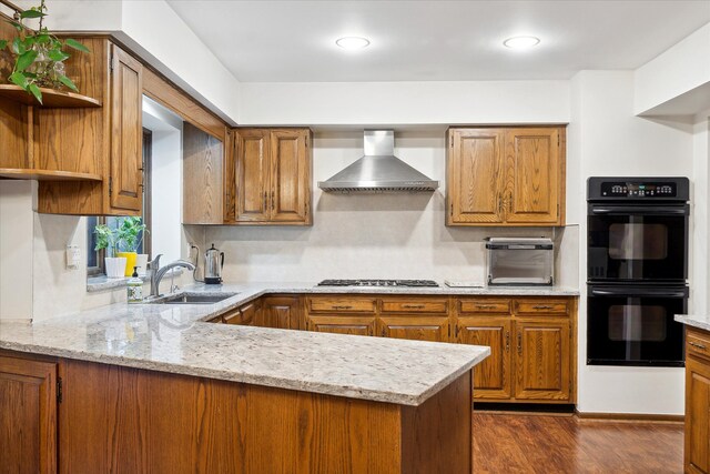 kitchen featuring kitchen peninsula, wall chimney exhaust hood, black double oven, stainless steel gas stovetop, and dark hardwood / wood-style flooring