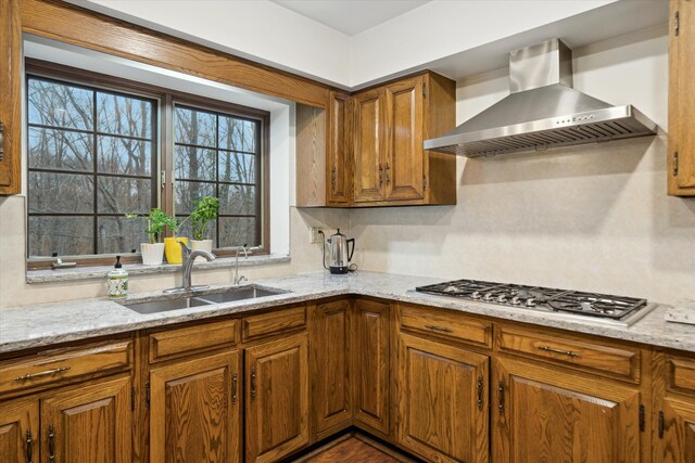 kitchen featuring stainless steel gas cooktop, light stone counters, decorative backsplash, sink, and wall chimney range hood