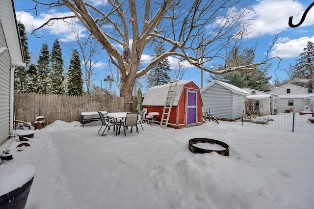 yard layered in snow featuring an outdoor fire pit and a storage unit