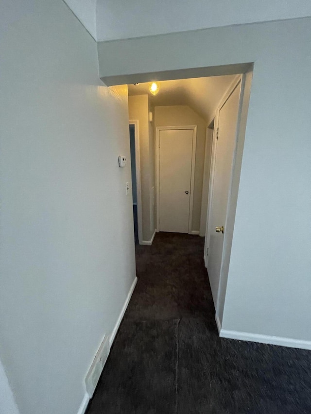 corridor featuring vaulted ceiling and dark carpet