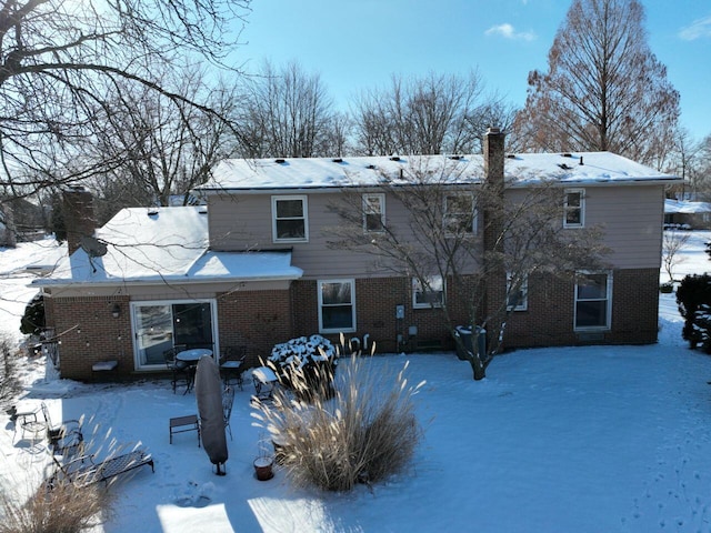 snow covered back of property featuring a chimney and brick siding