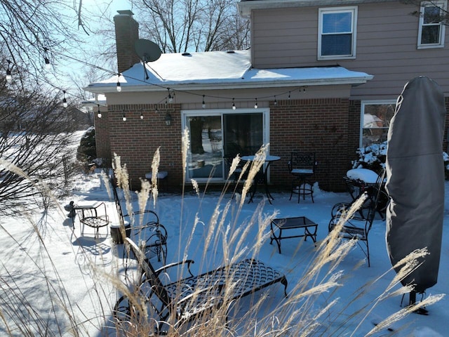 snow covered property with a patio, brick siding, and a chimney