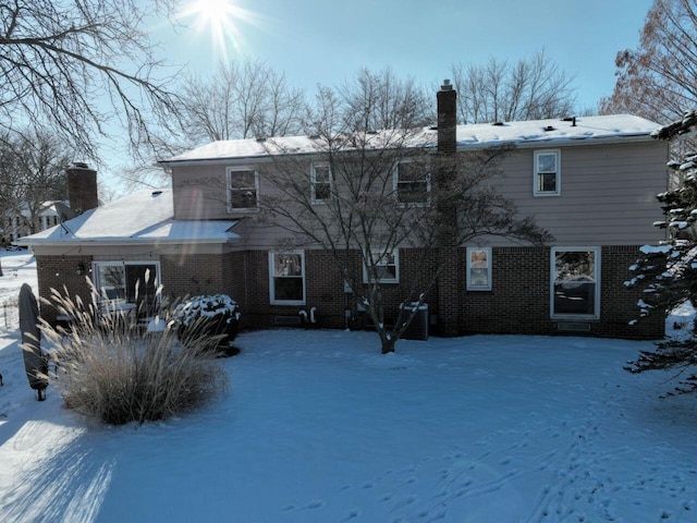 snow covered house with brick siding and a chimney