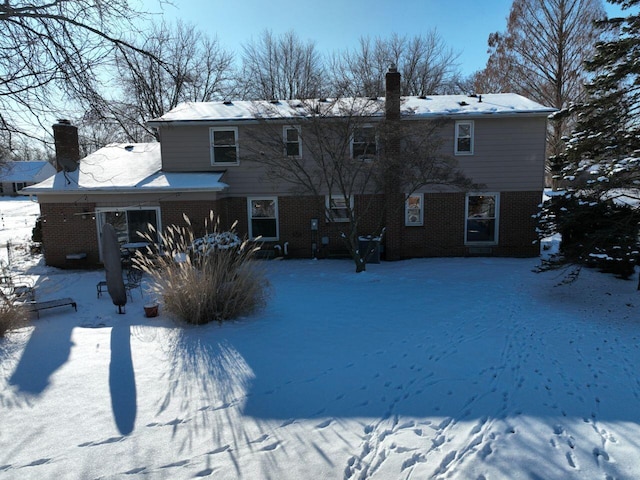 snow covered property featuring a chimney and brick siding