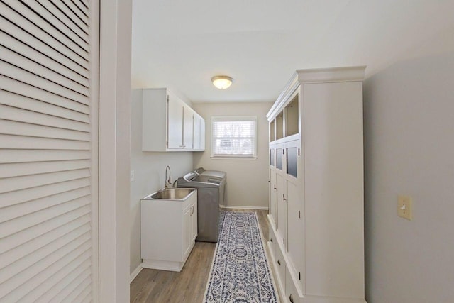 laundry room with cabinet space, light wood finished floors, a sink, baseboards, and washer and clothes dryer