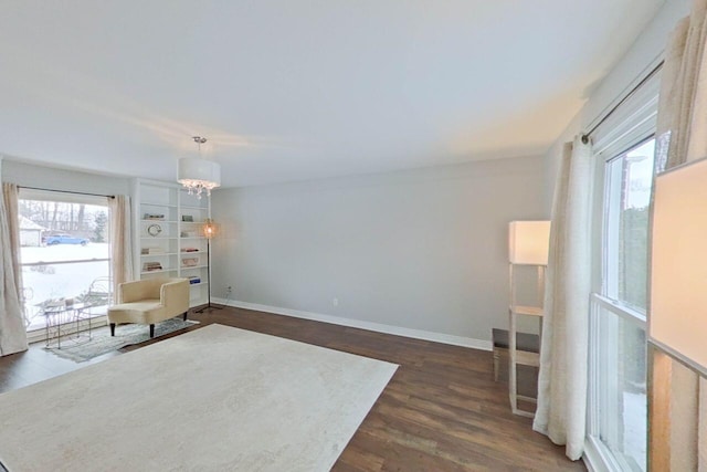 living area with dark wood-type flooring, a healthy amount of sunlight, a notable chandelier, and baseboards
