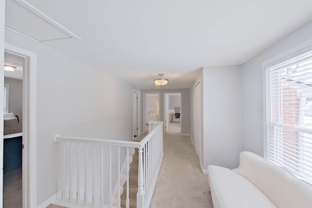 corridor featuring attic access, an upstairs landing, light carpet, and baseboards