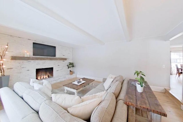 living room with baseboards, beamed ceiling, wood finished floors, and a brick fireplace
