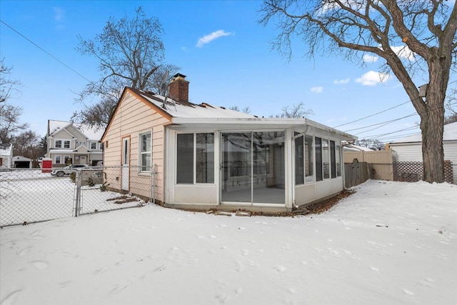 snow covered rear of property with a sunroom