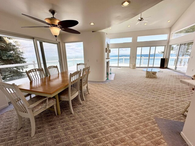 carpeted dining space with lofted ceiling, ceiling fan, and a water view