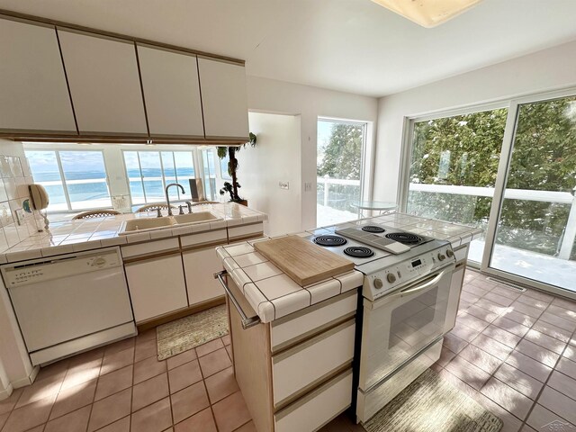 kitchen featuring sink, white cabinets, tile countertops, a water view, and white appliances