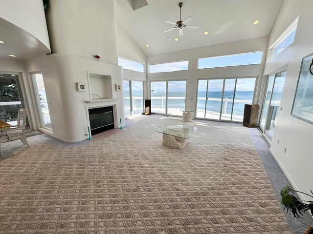 unfurnished living room featuring a towering ceiling, carpet floors, and a water view