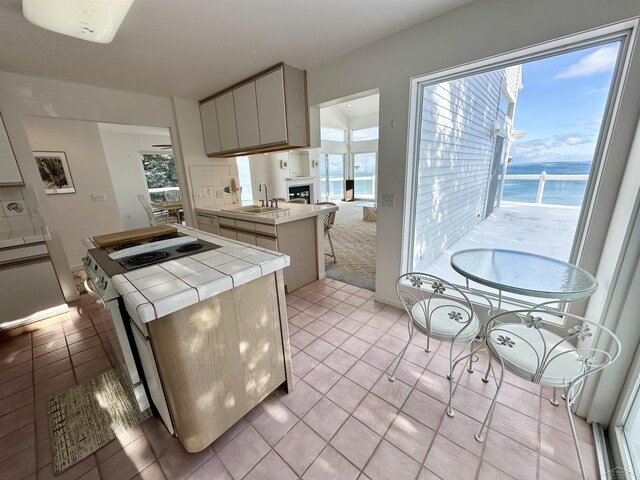 kitchen featuring tile counters, a center island, a water view, light tile patterned floors, and sink