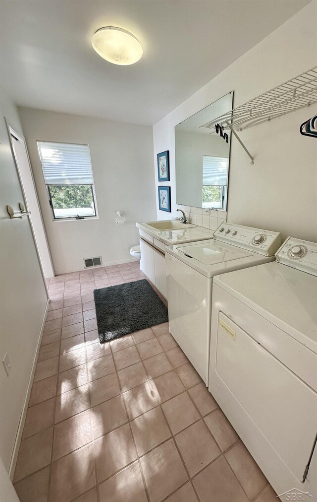 clothes washing area with sink, washer and clothes dryer, light tile patterned floors, and cabinets