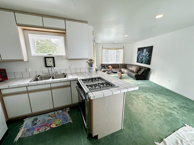 kitchen with sink, tile countertops, kitchen peninsula, stainless steel gas stovetop, and dark colored carpet