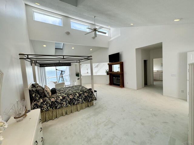 carpeted bedroom with ceiling fan, ensuite bathroom, multiple windows, and a high ceiling