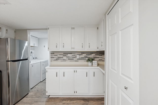 kitchen featuring stainless steel fridge, light hardwood / wood-style flooring, white cabinetry, tasteful backsplash, and washing machine and clothes dryer