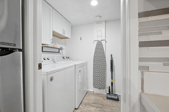 clothes washing area with light hardwood / wood-style floors, washer and dryer, and a textured ceiling