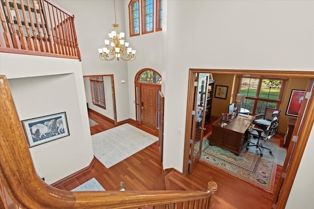 foyer entrance with an inviting chandelier, a towering ceiling, and wood-type flooring