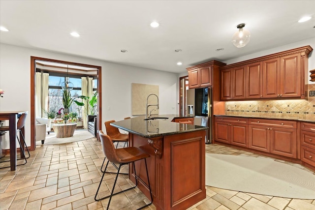 kitchen featuring a breakfast bar area, an island with sink, dark stone counters, decorative backsplash, and sink