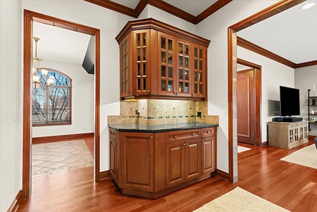 bar with hardwood / wood-style floors, crown molding, dark stone counters, decorative backsplash, and an inviting chandelier