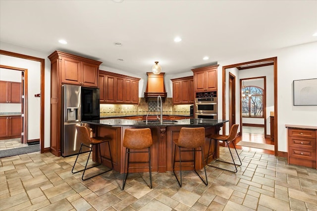 kitchen with a kitchen breakfast bar, dark stone countertops, a kitchen island with sink, appliances with stainless steel finishes, and backsplash