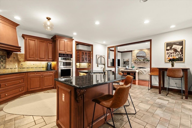 kitchen with sink, double oven, a kitchen bar, and a kitchen island with sink