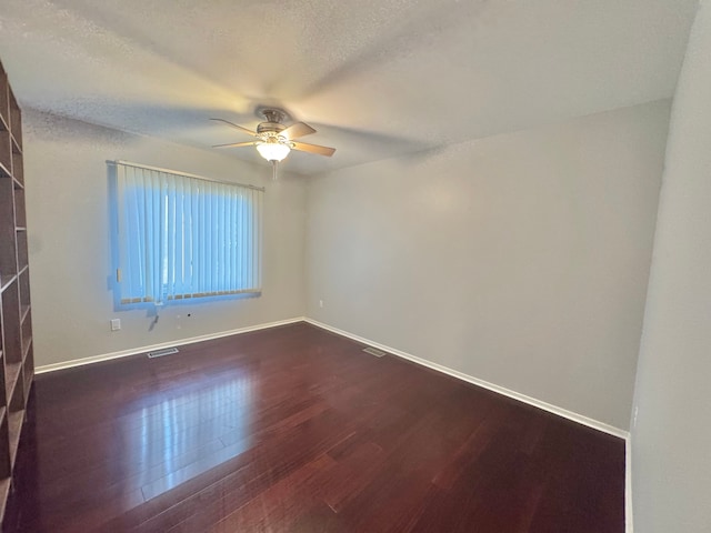 spare room with dark wood-style floors, visible vents, baseboards, and ceiling fan