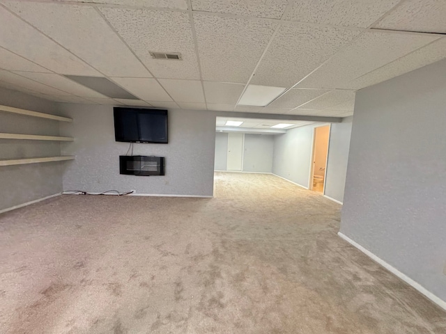 finished below grade area featuring carpet floors, a paneled ceiling, visible vents, a glass covered fireplace, and baseboards