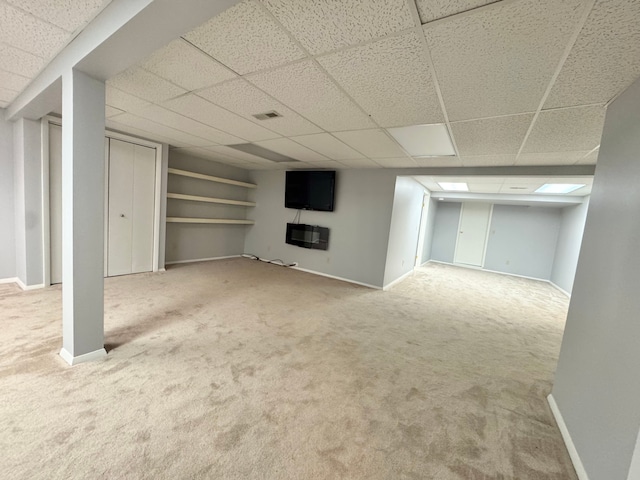 finished basement with baseboards, visible vents, a paneled ceiling, heating unit, and carpet floors