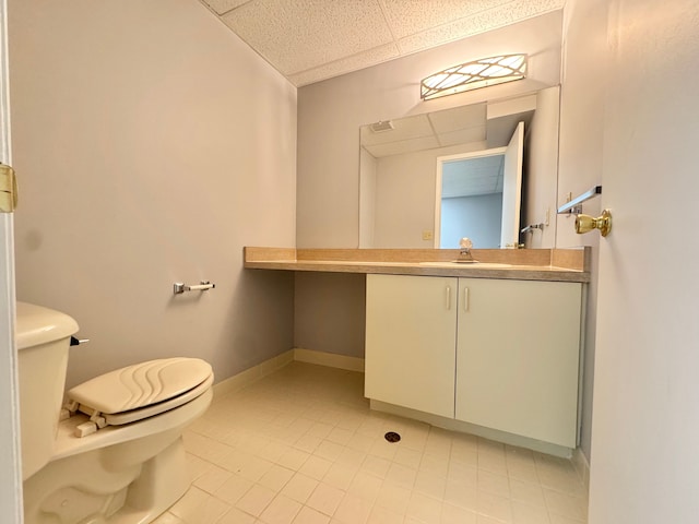 bathroom with a paneled ceiling, vanity, toilet, and baseboards