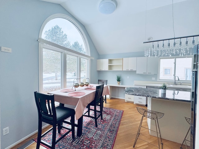 dining area with high vaulted ceiling, light wood-type flooring, visible vents, and baseboards