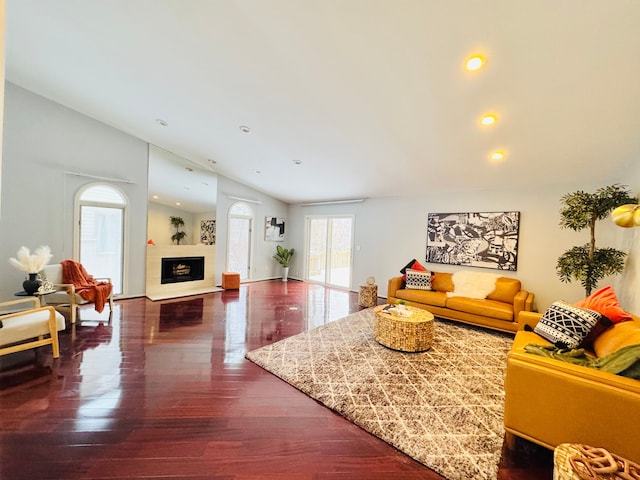 living room with a fireplace with raised hearth, vaulted ceiling, wood finished floors, and recessed lighting