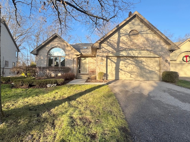 view of front of house with aphalt driveway, a front yard, brick siding, and a garage