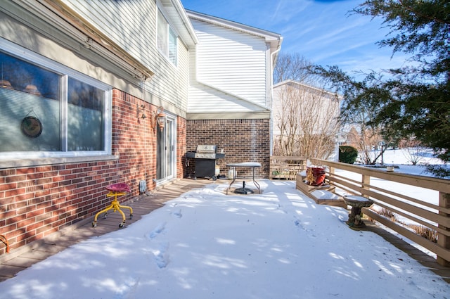 snow covered patio featuring grilling area and a deck