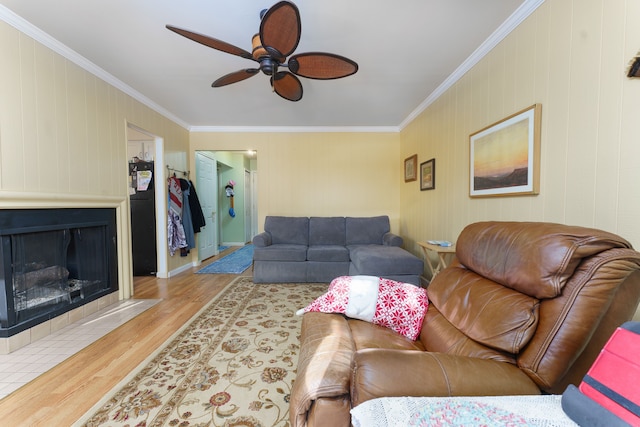 living room featuring crown molding, ceiling fan, a large fireplace, and light hardwood / wood-style floors