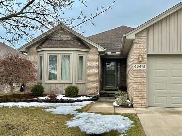 snow covered property entrance with a garage, brick siding, board and batten siding, and roof with shingles