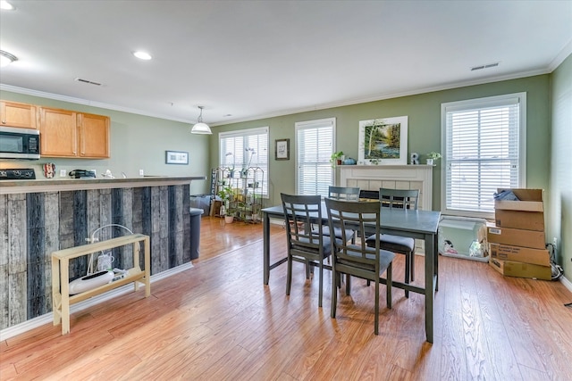 dining room with a fireplace, light wood-type flooring, and crown molding