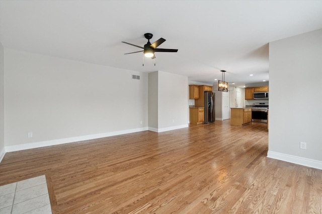 unfurnished living room featuring light wood-type flooring and ceiling fan with notable chandelier