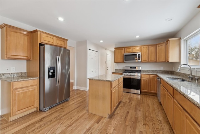 kitchen with light hardwood / wood-style floors, sink, a kitchen island, stainless steel appliances, and light stone counters