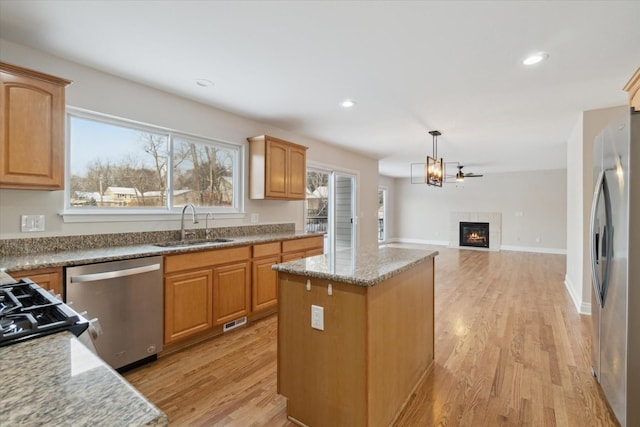 kitchen featuring appliances with stainless steel finishes, hanging light fixtures, sink, a kitchen island, and light wood-type flooring