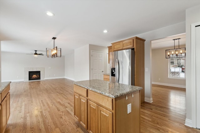 kitchen with pendant lighting, a center island, light hardwood / wood-style flooring, stainless steel refrigerator with ice dispenser, and a tile fireplace