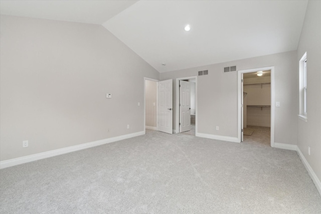 unfurnished bedroom with a walk in closet, vaulted ceiling, light colored carpet, and a closet