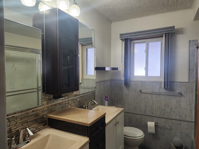 bathroom featuring toilet, vanity, tile walls, decorative backsplash, and a textured ceiling