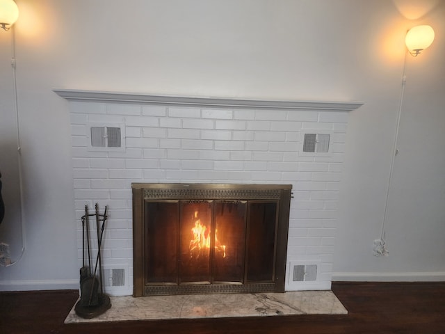 room details with visible vents, a fireplace, baseboards, and wood finished floors