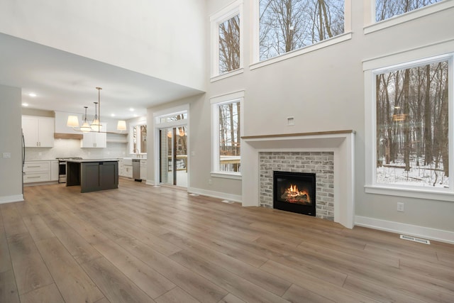 unfurnished living room with a towering ceiling, a fireplace, and light hardwood / wood-style floors