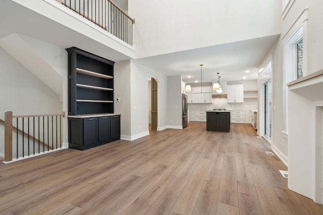 unfurnished living room featuring a towering ceiling, light wood-type flooring, and built in features