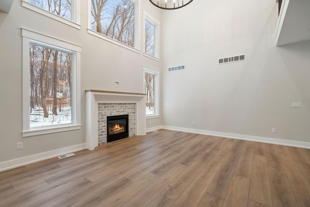 unfurnished living room with a high ceiling, light wood-type flooring, a brick fireplace, and a notable chandelier